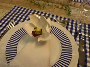 Orquídea branca sobre guardanapo de tecido em mesa posta azul com formas circulares e delicadas.