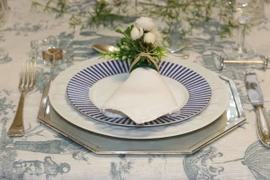 composicao-de-mesa-posta-com-sousplat-dourado-prato-azul-listrado-e-guardanapo-de-linho-branco