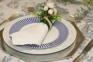 mesa-posta-elegante-com-sousplat-dourado-prato-branco-e-azul-e-guardanapo-de-linho-com-porta-guardanapo-floral