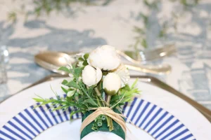 porta guardanapo com flores brancas sobre guardanapo de linho em mesa posta elegante com prato azul listrado