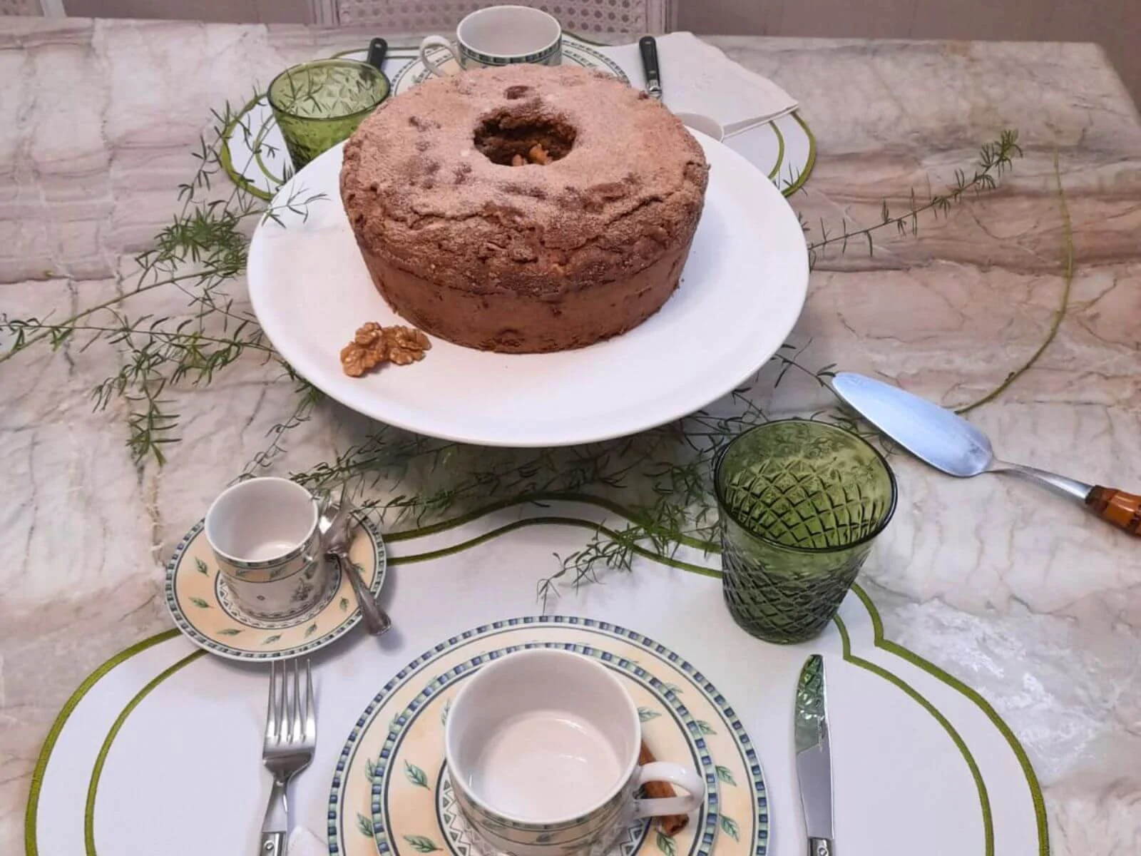 mesa-posta-elegante-com-louca-classica-em-tons-de-verde-e-branco-bolo-caseiro-ao-centro-e-composicao-leve-sobre-mesa-de-marmore