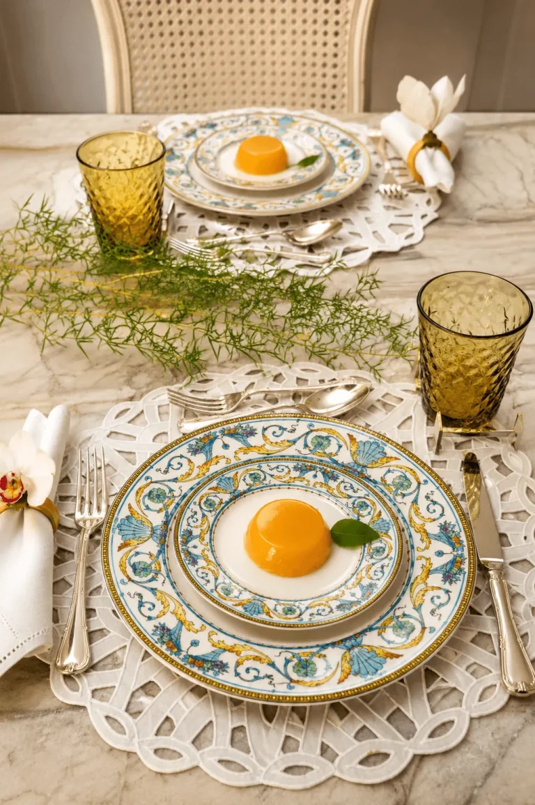 Mesa-posta-elegante-com-louca-Mikasa-azul-e-amarela-copos-Balloton-Maca-Verde-Zafferano-folhagens-naturais-e-quindim-sobre-mesa-de-marmore.