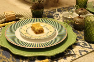 Baklava servida em prato decorado sobre composição azul e verde inspirada na natureza.