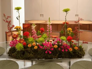 Centro de mesa com flores em tons de rosa, vermelho, coral e verde criando uma paisagem orgânica para receber convidados.