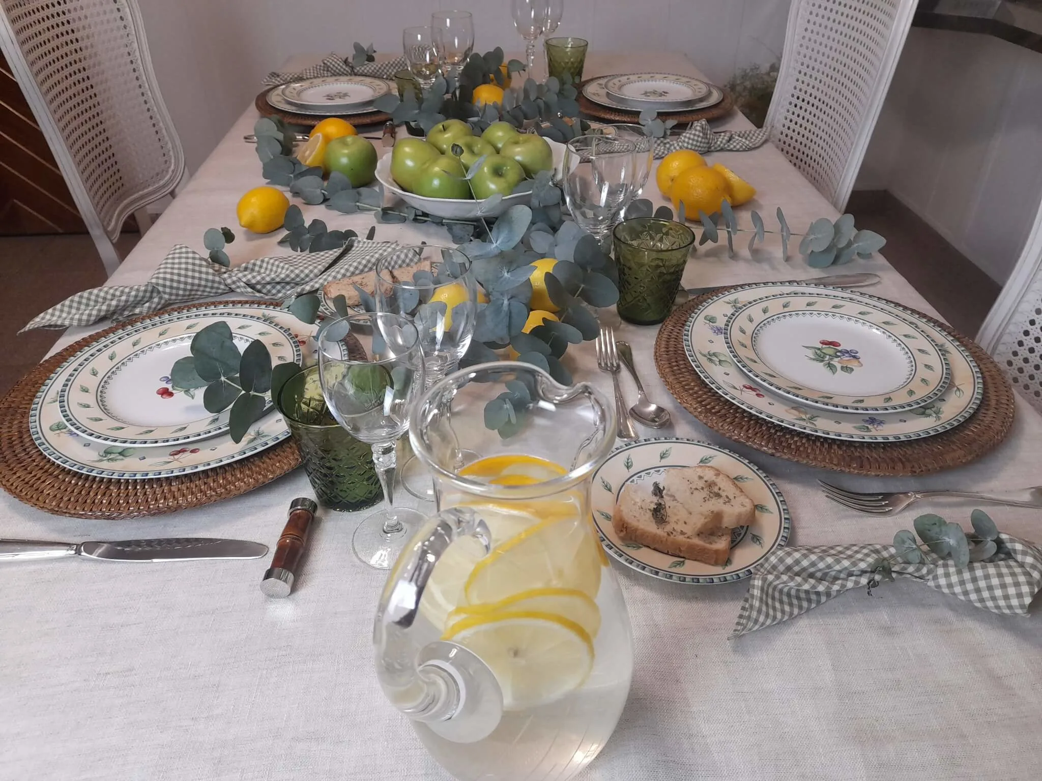 Mesa posta com limões sicilianos, maçãs verdes e eucalipto em composição natural sobre mesa de jantar elegante